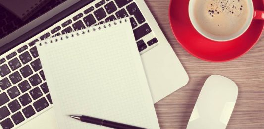 Blank notepad over laptop and coffee cup on office wooden table
